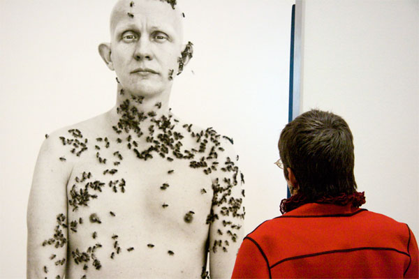 At Richard Avedon exhibition SFMoMA Oct. 2009 Woman in Red coat stands in front of a portrait of a naked beekeeper with bees crawling over his body and face